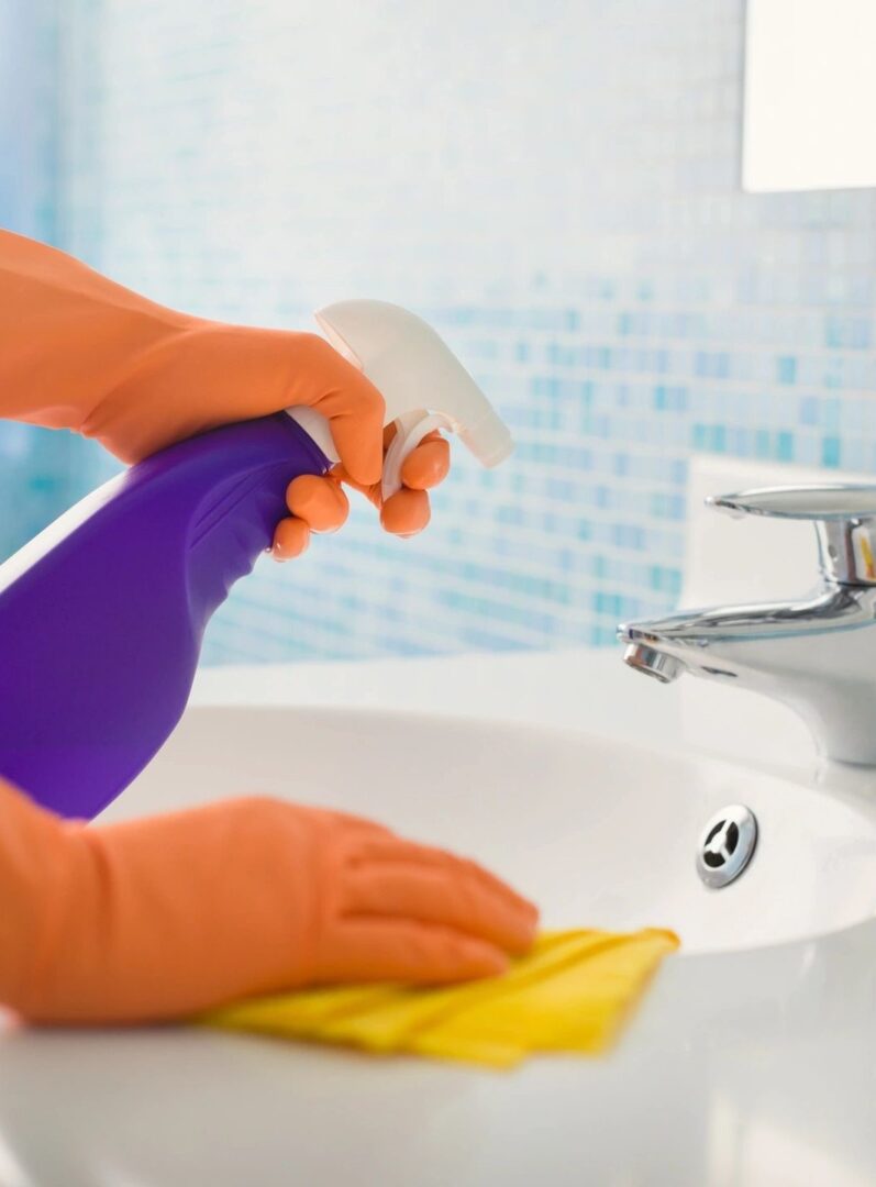 A person cleaning the bathroom sink with gloves on.