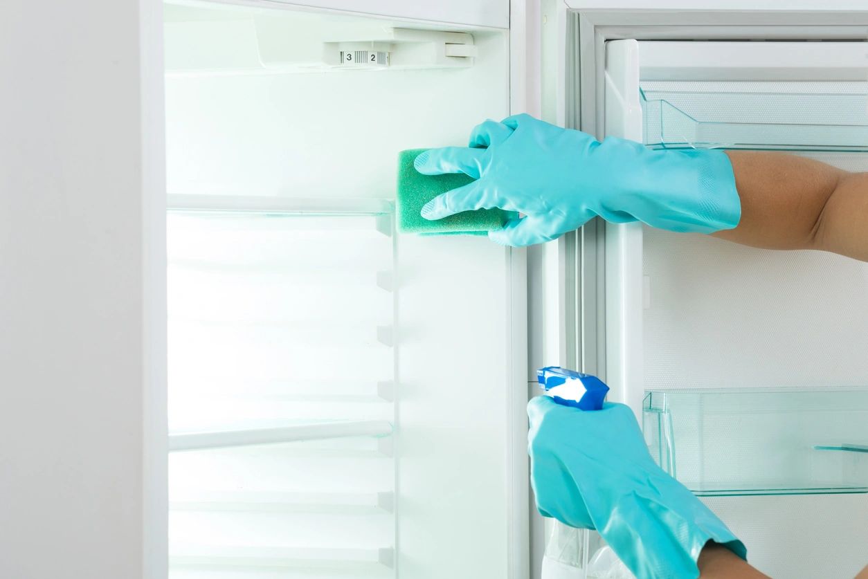 A person wearing gloves and cleaning the inside of an open refrigerator.